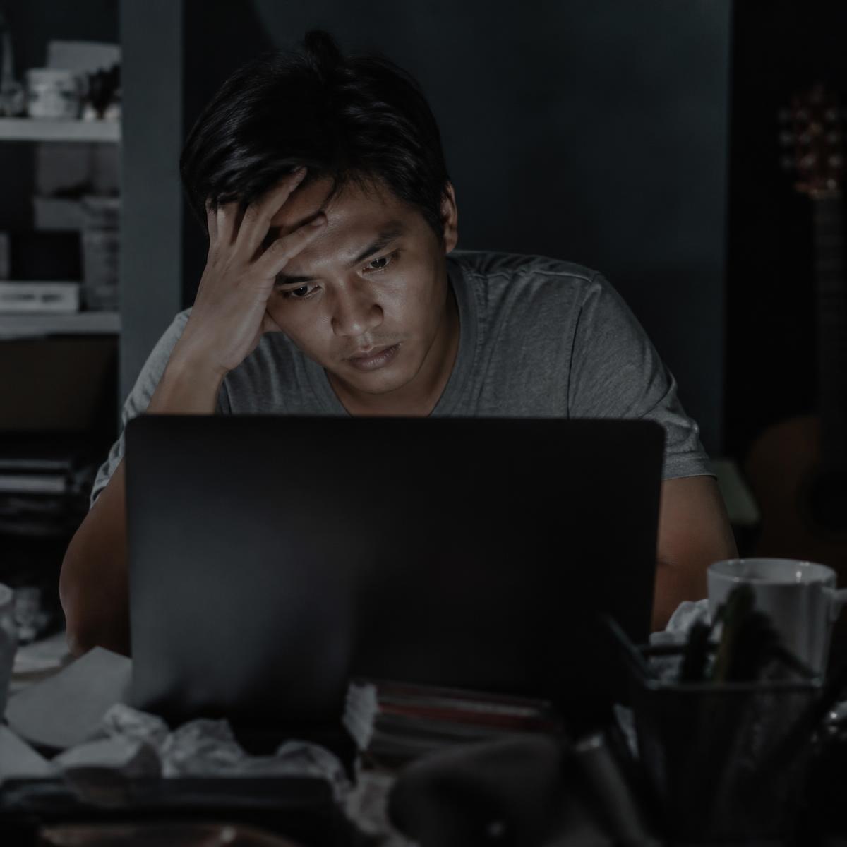 Freelancer looking frustrated at a laptop in a dim room