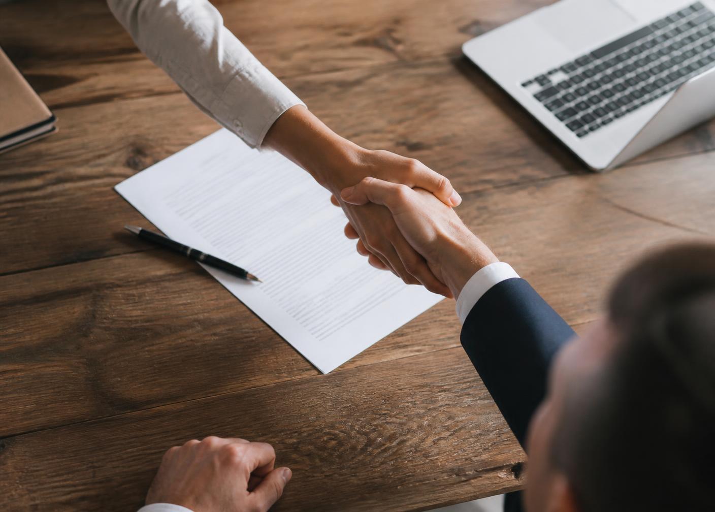 Overhead view of a handshake over a signed contract beside a laptop